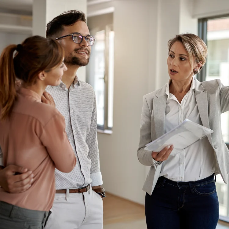 pareja de esposos recibiendo la guía de una agente inmobiliaria mientras observan un apartamento